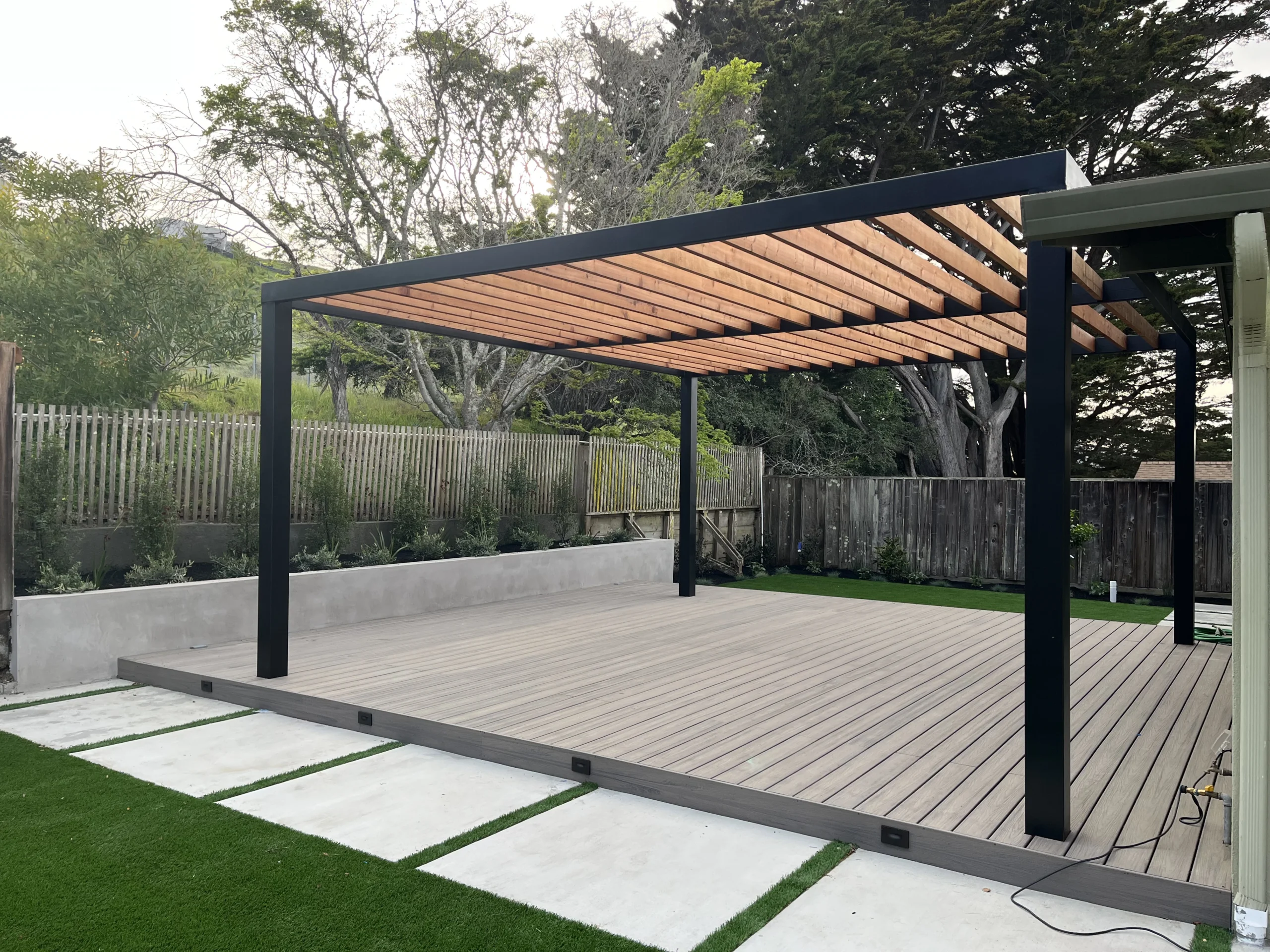 Composite deck and pergola beside a concrete planter wall